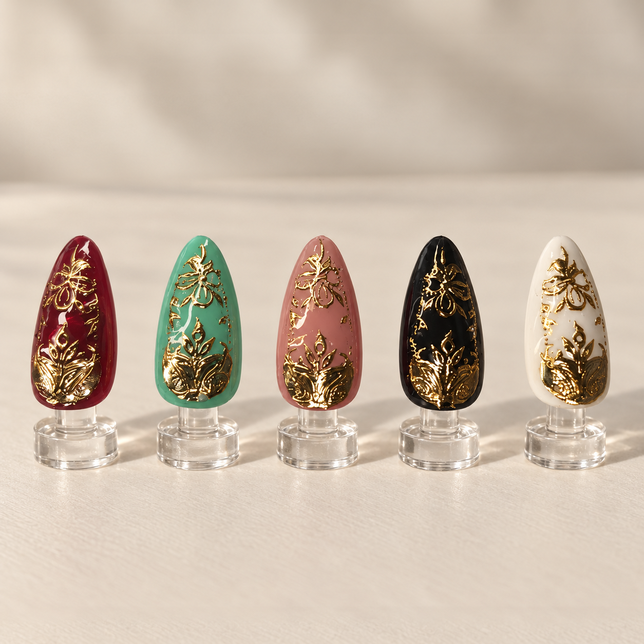 Jewel toned nail art with ornate raised gold floral details displayed on clear stands