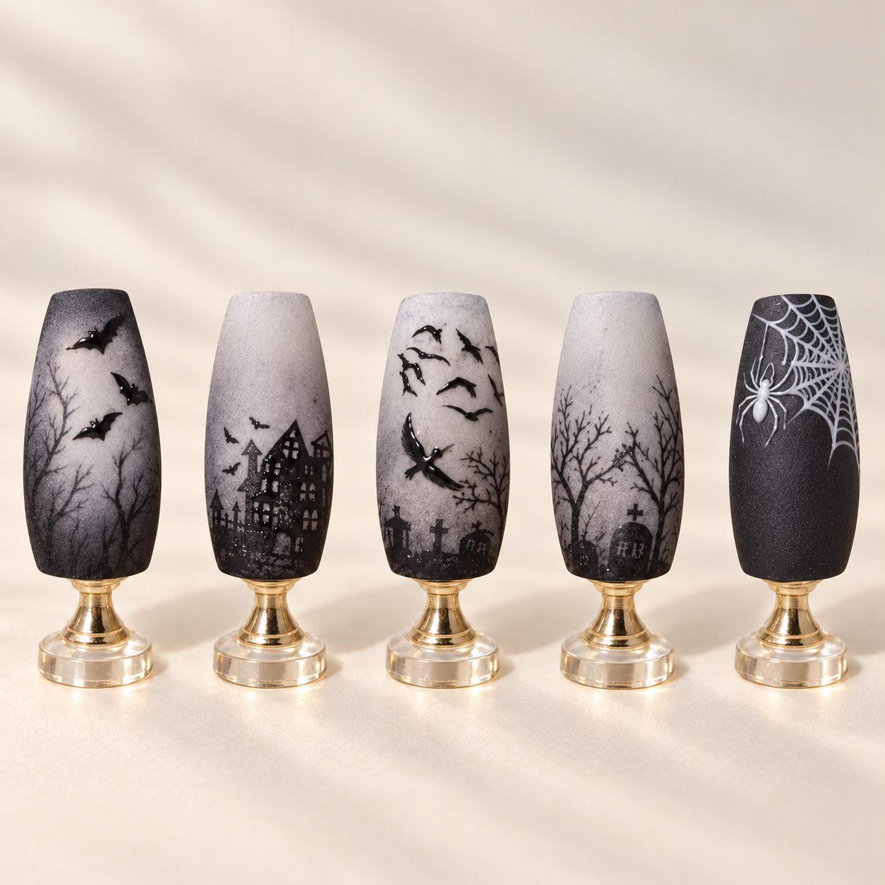 Monochrome graveyard nail art with bats birds haunted houses bare trees tombstones and a spiderweb displayed upright on gold stands