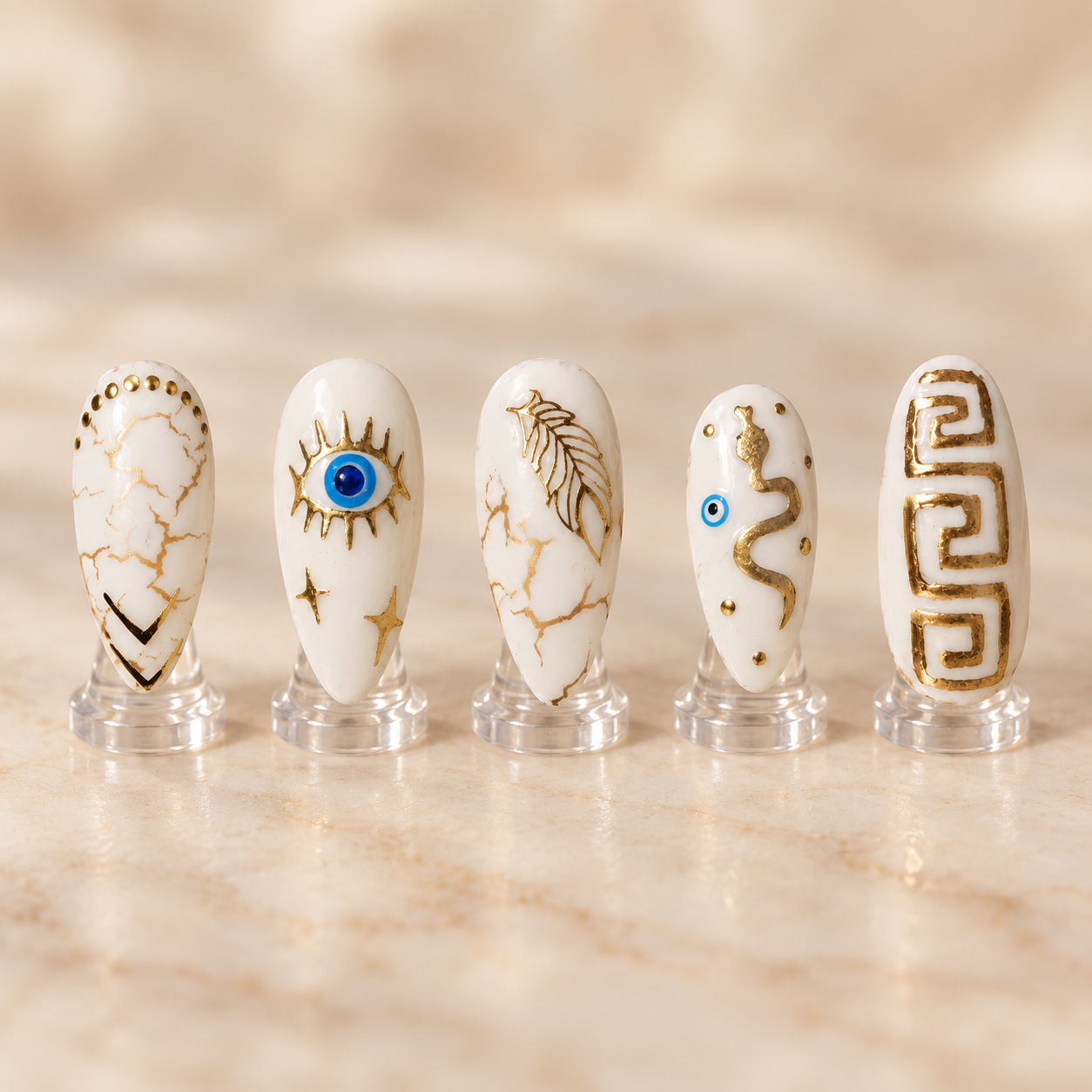 Ivory and gold Greek inspired nail art with marble evil eye key and serpent details displayed on clear stands