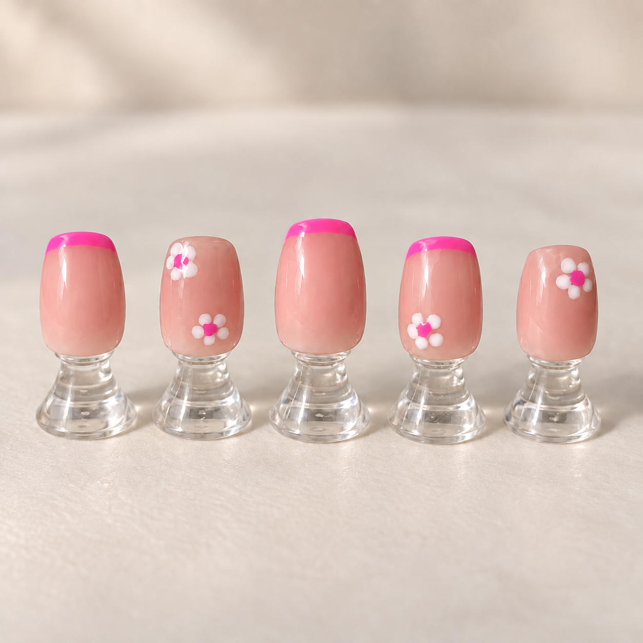 Blush pink daisy nail art with hot pink French accents displayed on clear stands