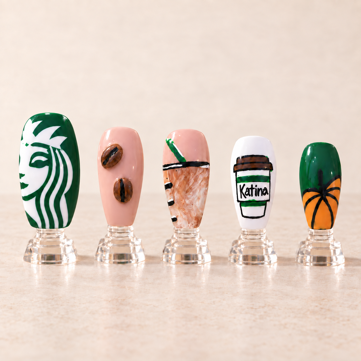 Coffee themed fall nail art with coffee beans an iced macchiato a personalized takeaway cup and a pumpkin displayed upright on clear stands